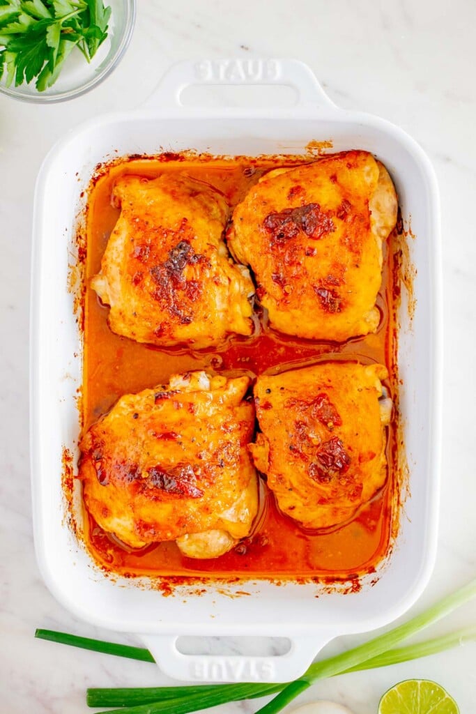 Fully cooked honey chipotle chicken thighs in a white baking dish with fresh parsley and green onions on the side 