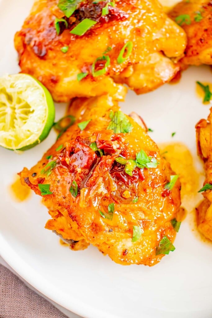 An overhead shot of a honey chipotle chicken thigh with more on the side on a white plate