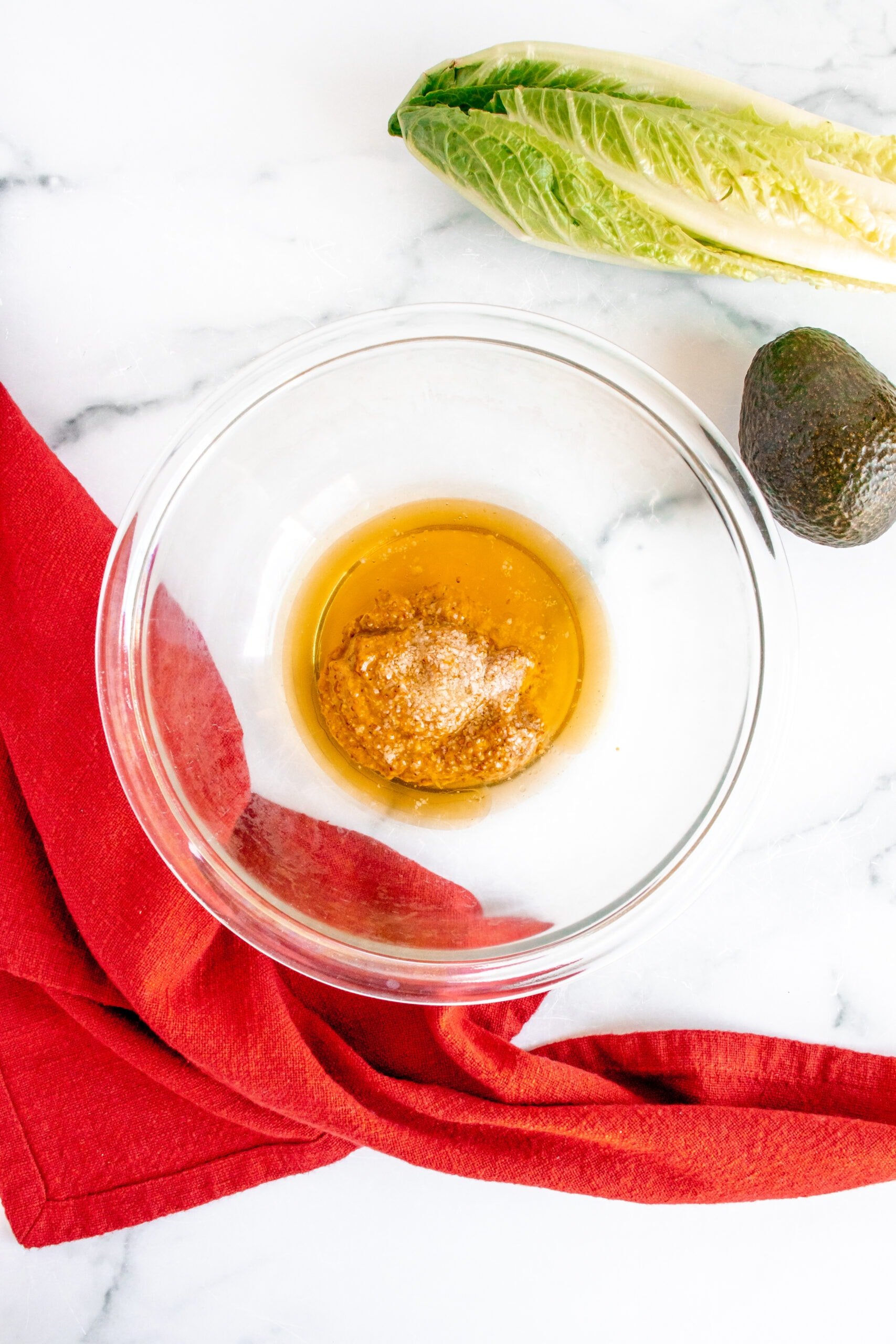ingredients for honey mustard dressing in a clear bowl before being mixed on a marble background with a tea towel on the side