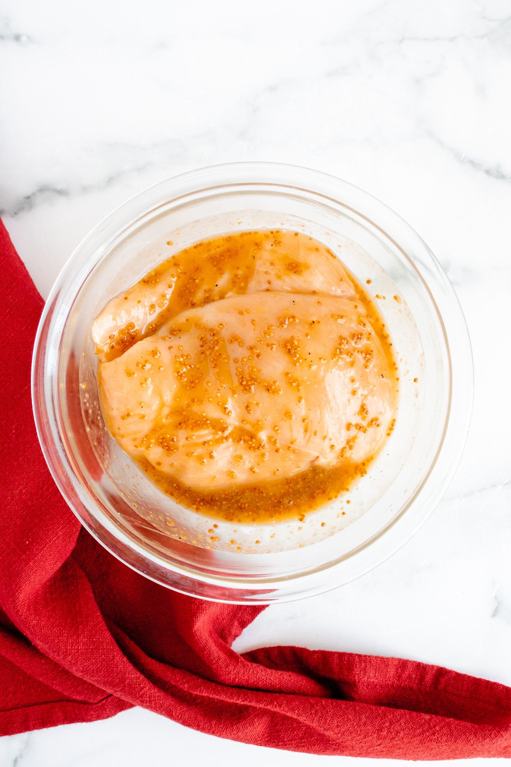 Chicken breast marinating in a honey mustard dressing in a clear bowl for a salad