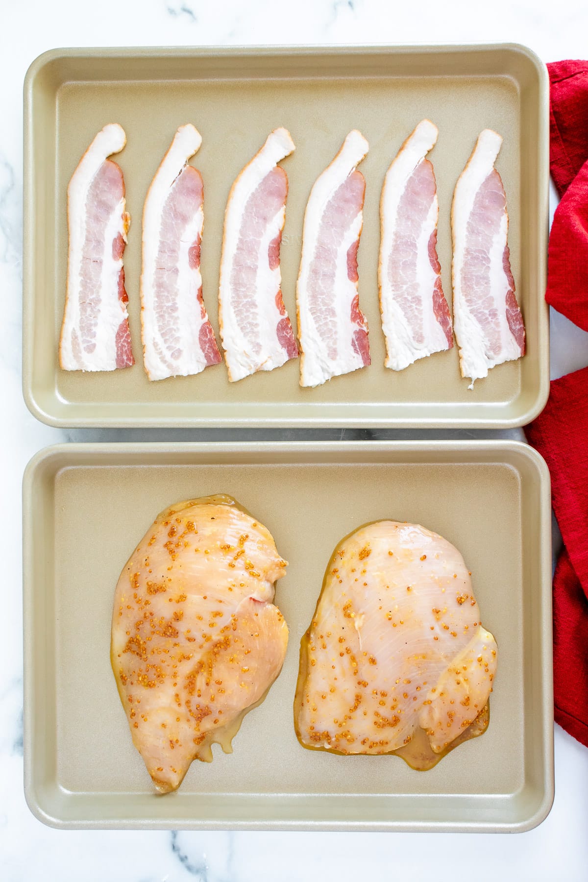 Two sheet pans: one with raw bacon and one with raw honey mustard marinated chicken for salad
