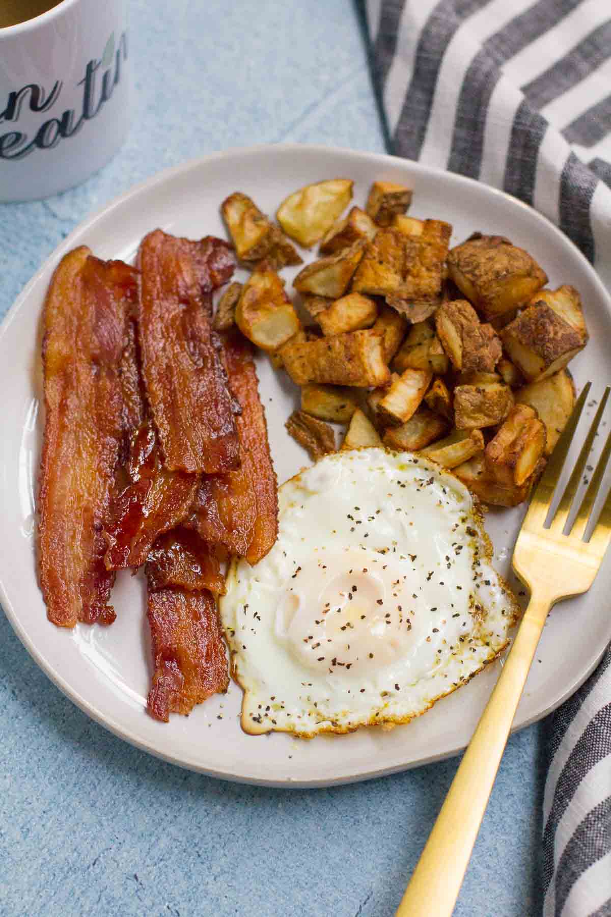 How to Cook Crispy Bacon - showing bacon on white plate with potatoes and a fried egg.