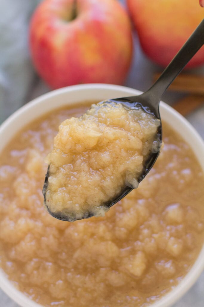 A bowl of pressure cooker applesauce with a black serving spoon taking a scoop out of it.