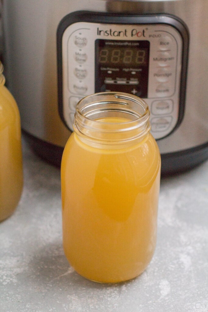 A glass mason jar filled with chicken bone broth in front of an instant pot.