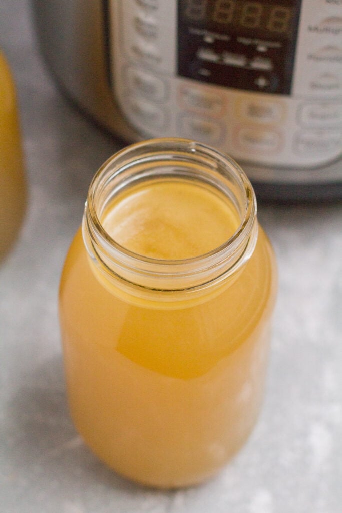 A glass jar of bone broth next to an instant pot