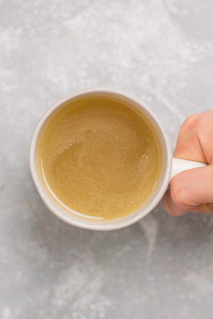 A hand holding a mug of instant pot chicken broth on a grey background