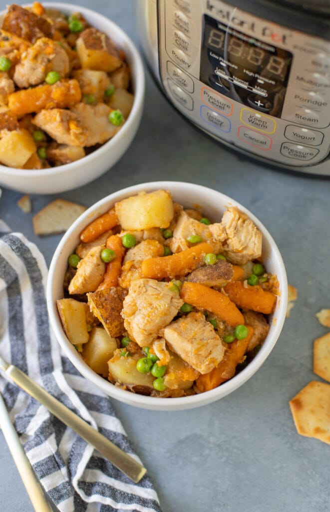 An overhead shot of instant pot chicken stew on a grey background with another bowl and instant pot to the side