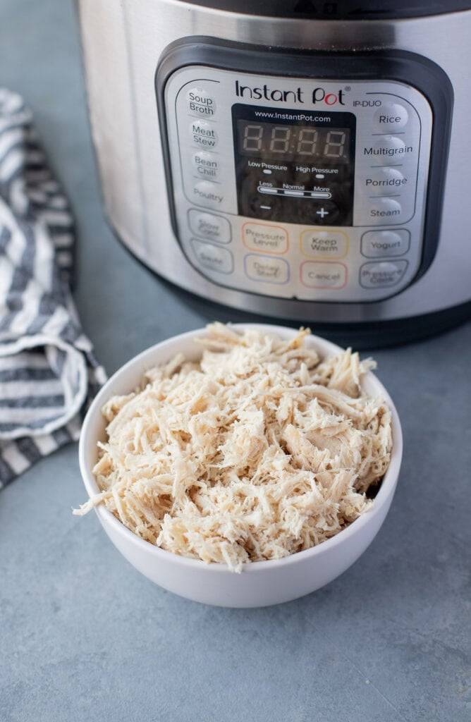 Easy Instant Pot Shredded Chicken in a blue bowl with a pressure cooker behind it