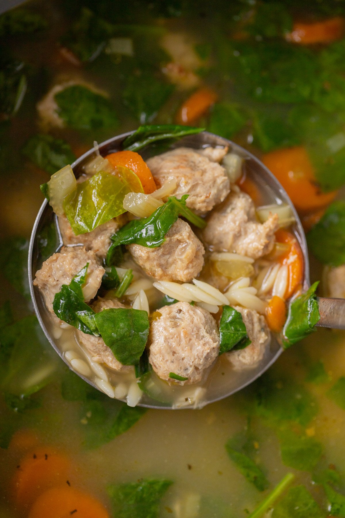 A ladle taking a large scoop of best italian wedding soup out of a pot
