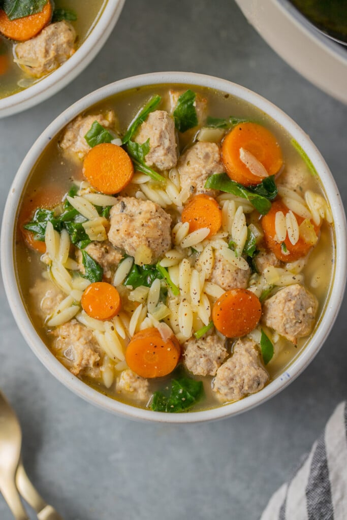 A close overhead shot of Italian wedding soup in a white bowl on a grey background