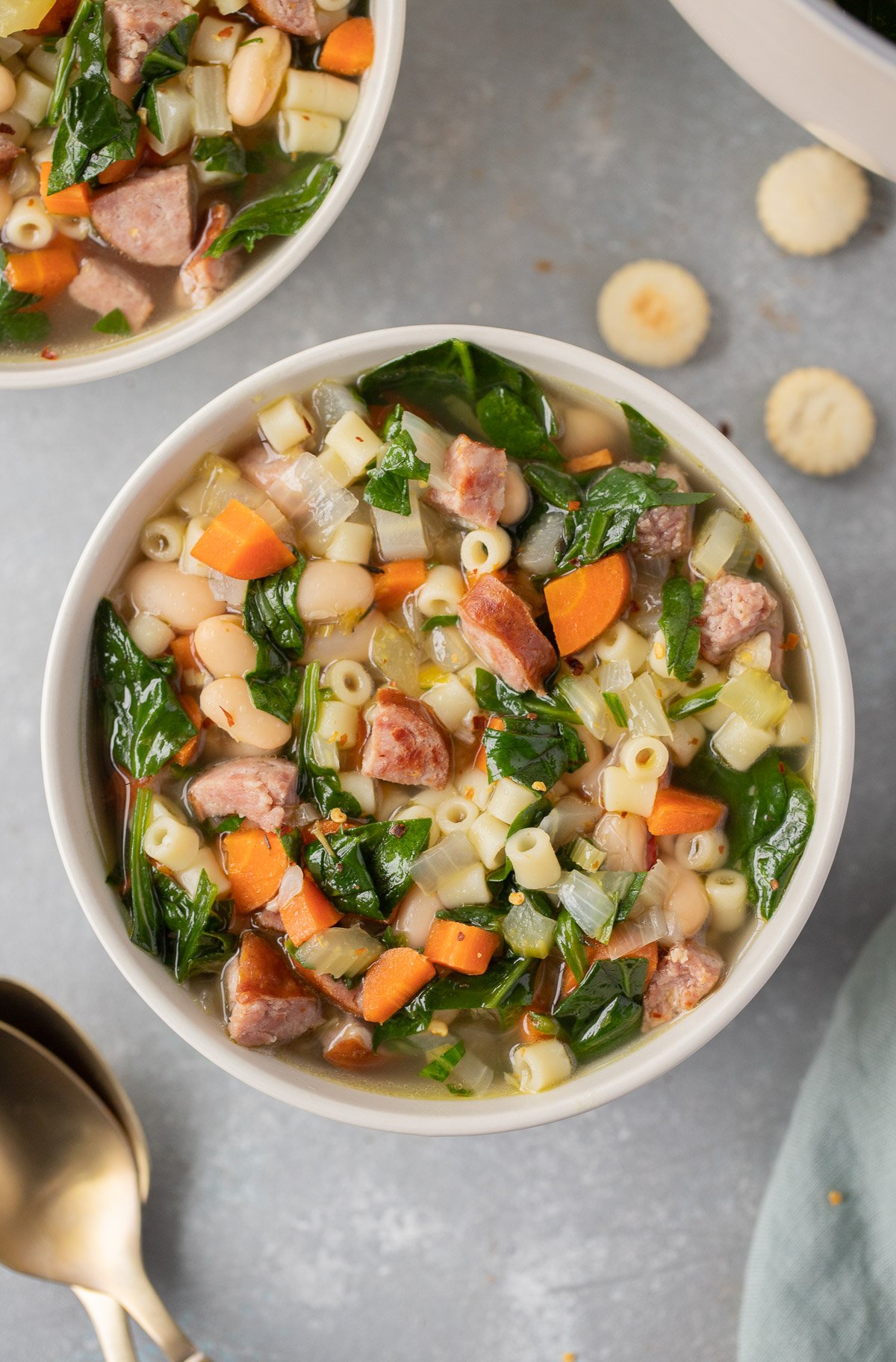 An overhead shot of a bowl of kielbasa soup with another bowl of soup and spoons on the side