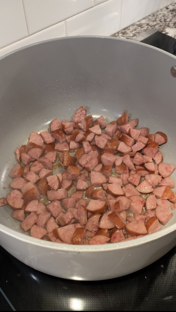 Kielbasa sausage browning in a large pot on a black stove