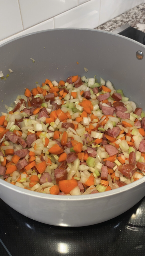 Veggies and kielbasa cooking in a large pot for polish sausage soup in a large pot on a black stove