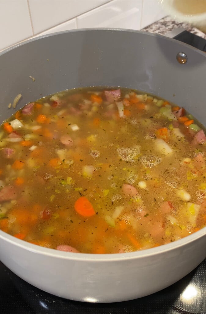 Kielbasa soup cooking in a large pot before the spinach and pasta has been added on a black stovetop