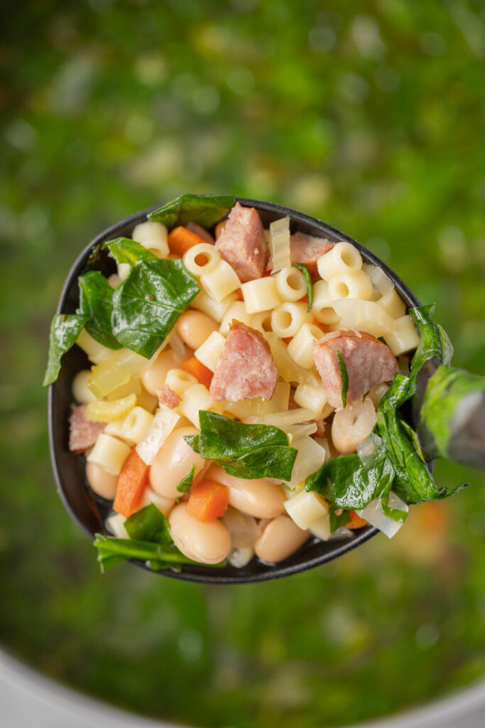 A black ladle scooping kielbasa soup out of a large pot of the soup in the background