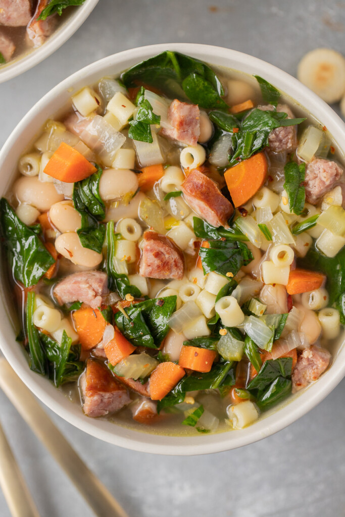 An overhead shot of a bowl of kielbasa soup on a grey background