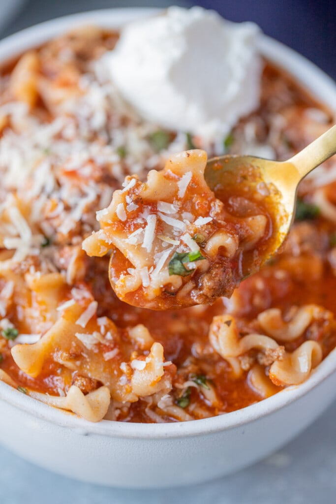 A gold spoon taking a bite out of a bowl of lasagna soup