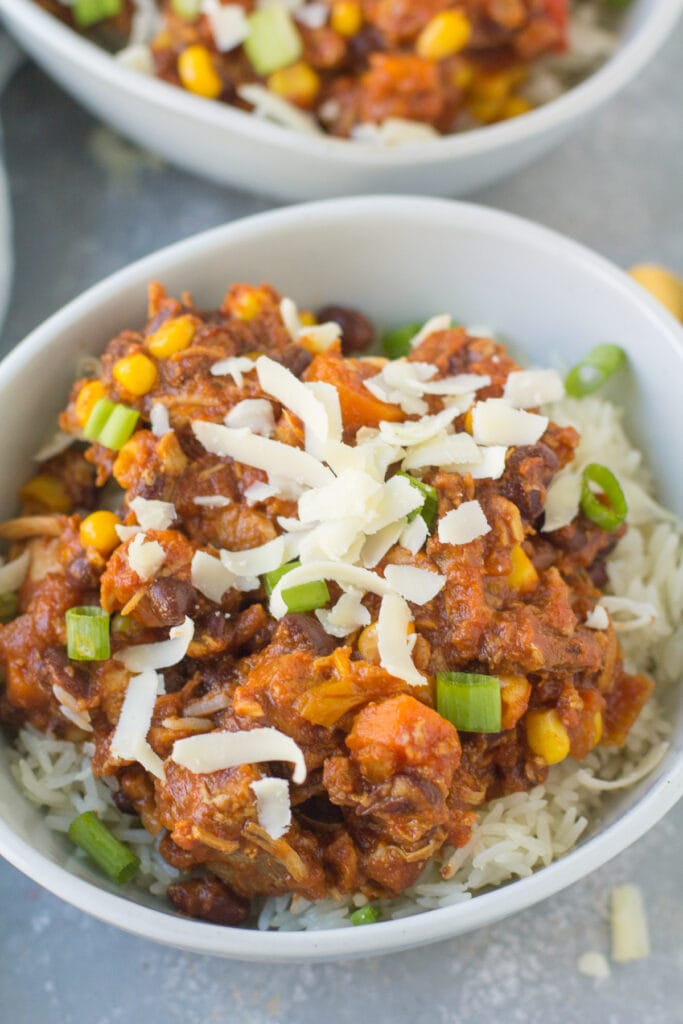 A close up Thanksgiving leftover chili in a bowl with rice, cheese and green onions