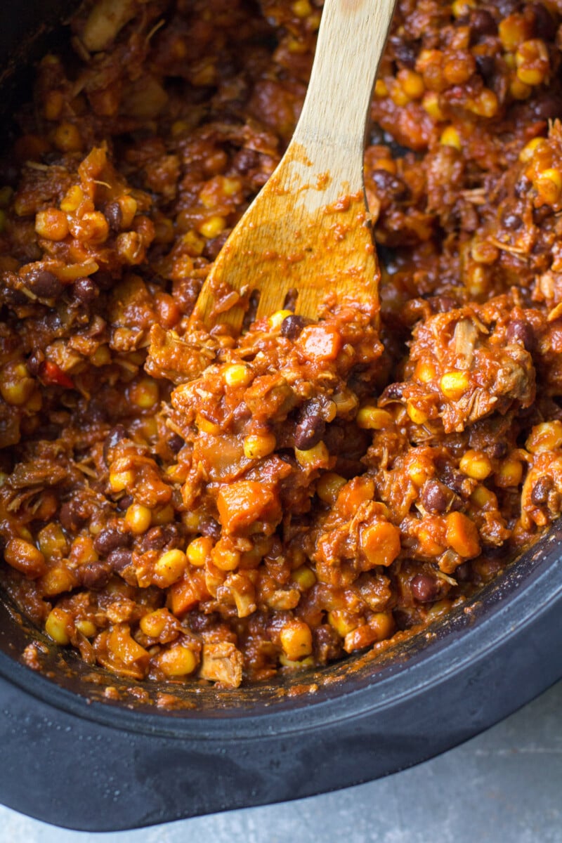 A wooden spoon stirring leftover turkey chili in a crockpot base.