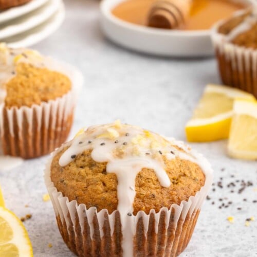Healthy Lemon Chia Seed Muffin topped with a glaze with more muffins and lemon slices in the background.