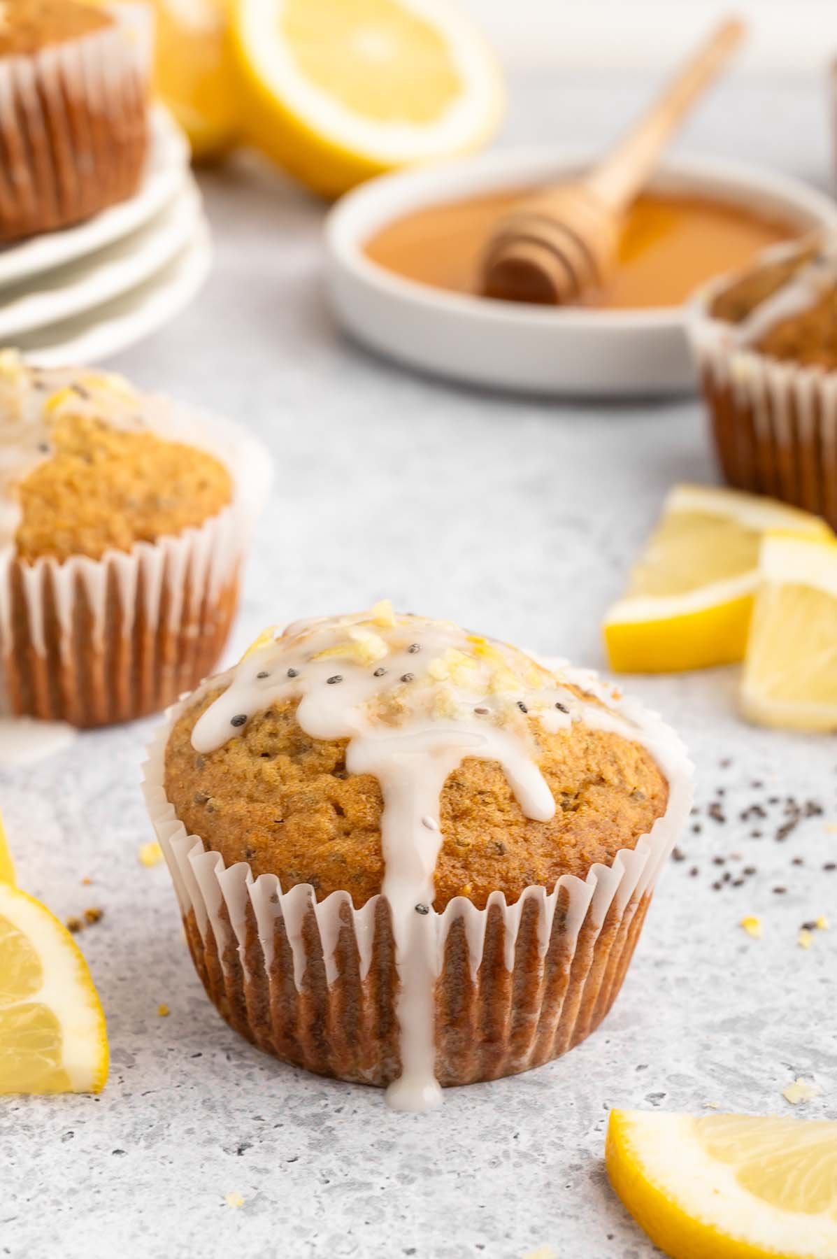 Healthy Lemon Chia Seed Muffin topped with a glaze with more muffins and lemon slices in the background.