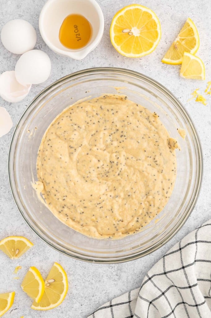 Lemon Chia Muffin Batter in a clear glass bowl with lemons on the side.
