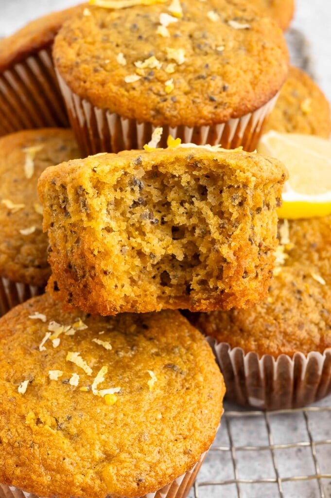 A lemon chia muffin with a bite out of it with more muffins in the background.