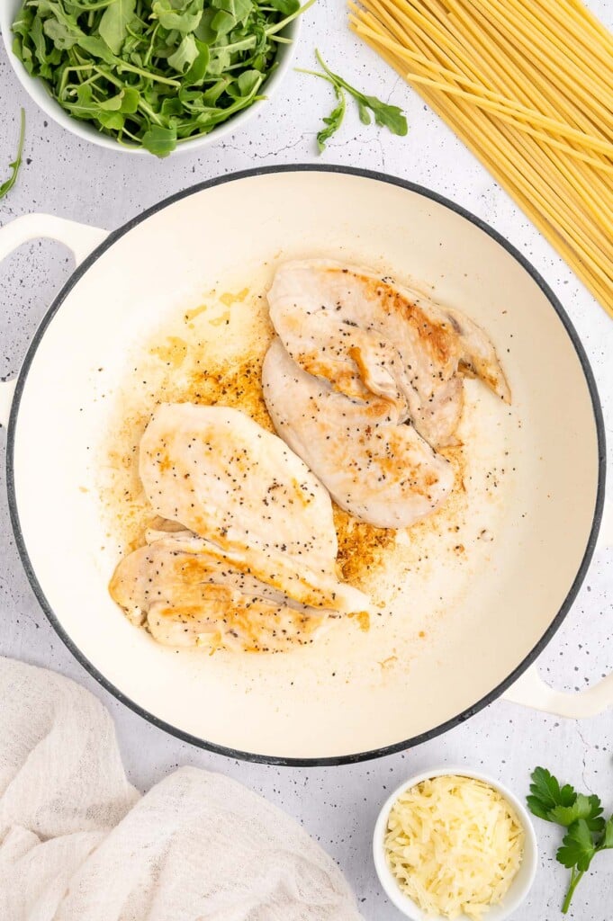 4 chicken breasts getting seared in a dutch oven with more ingredients for lemon chicken pasta on the side