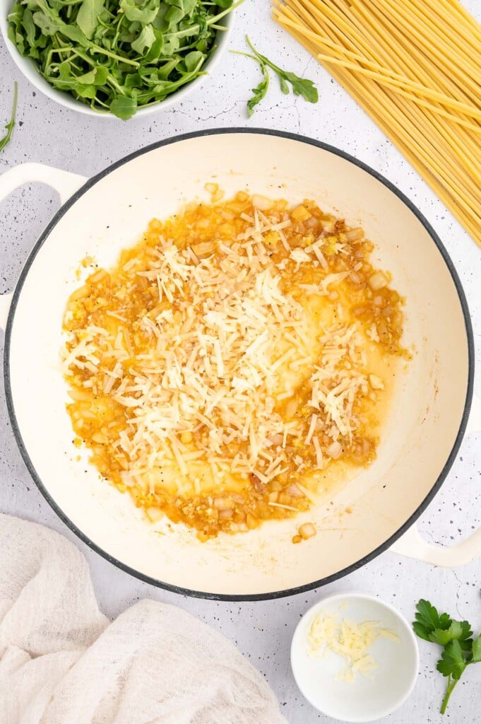 Cooked onion and garlic in avocado oil with lemon juice and parmesan cheese added in a dutch oven with more ingredients for lemon chicken pasta on the side