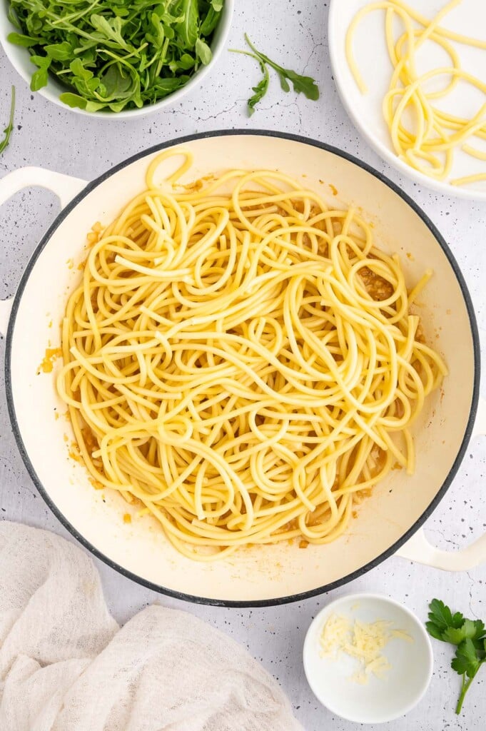 Bucatini pasta in a dutch oven with more ingredients for chicken lemon pasta on the side