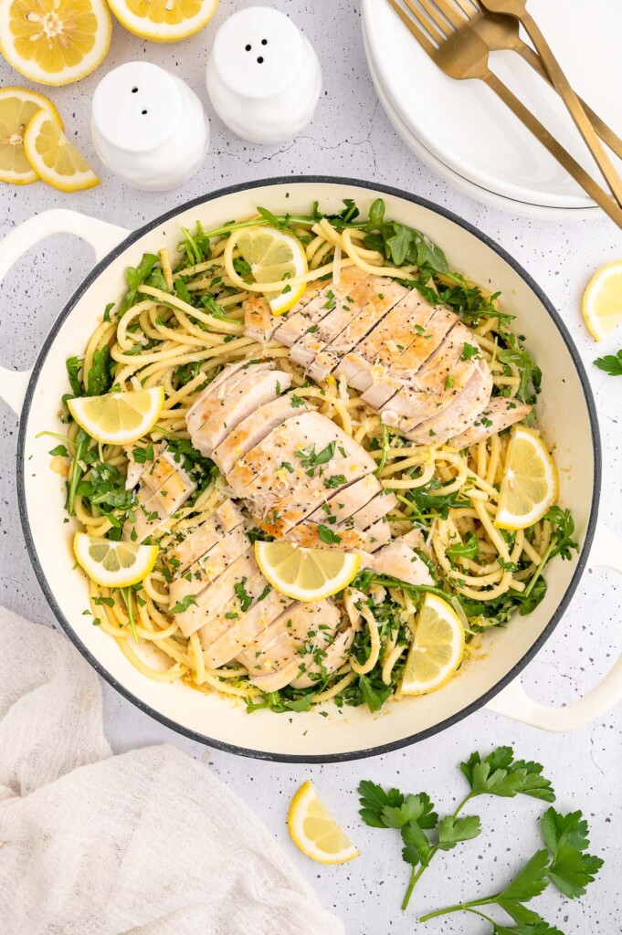 a dutch oven filled with lemon chicken pasta garnished with fresh parsley and lemon slices