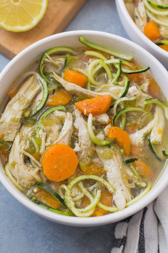 Lemon Chicken Soup in a white bowl on a blue background with a cutting board in the background