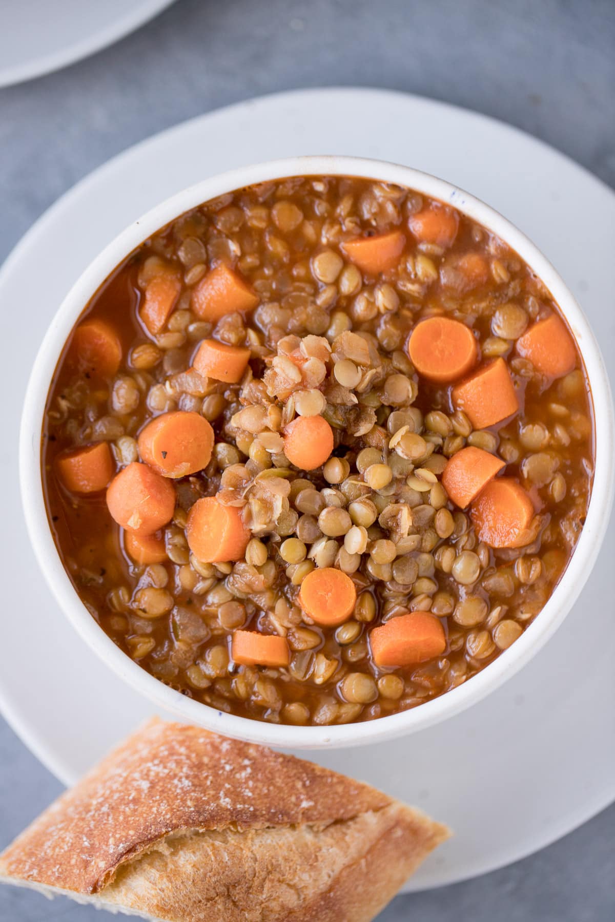 A bowl of easy lentil soup on a white plate with bread off to the side