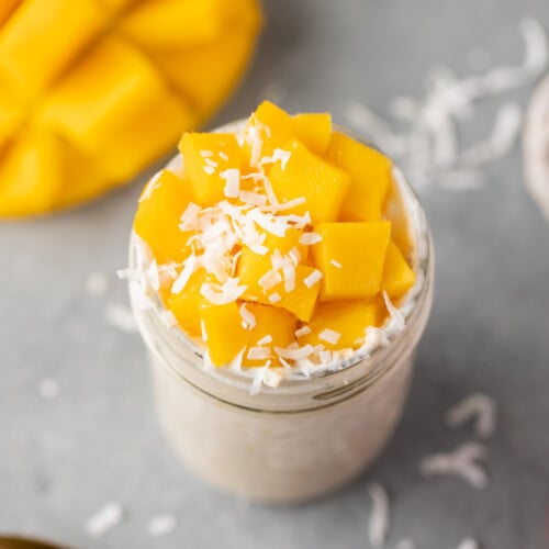 An overhead shot of mango overnight oats in a mason jar with a sliced mango in the background