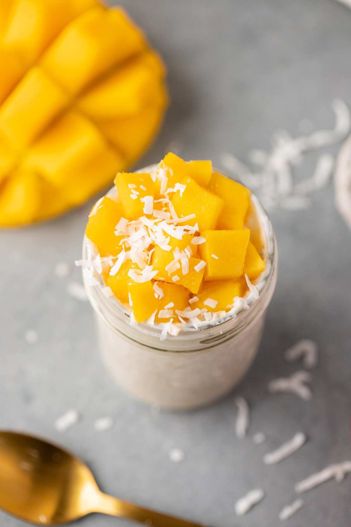 An overhead shot of mango overnight oats in a mason jar with a sliced mango in the background