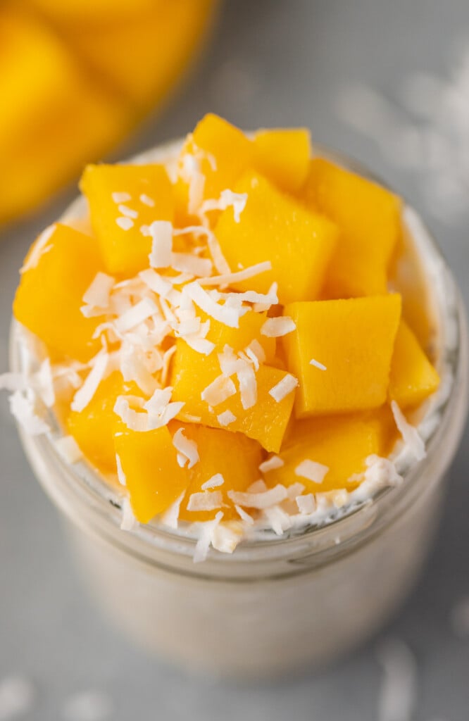 A close up of a mason jar of mango overnight oats on a grey background