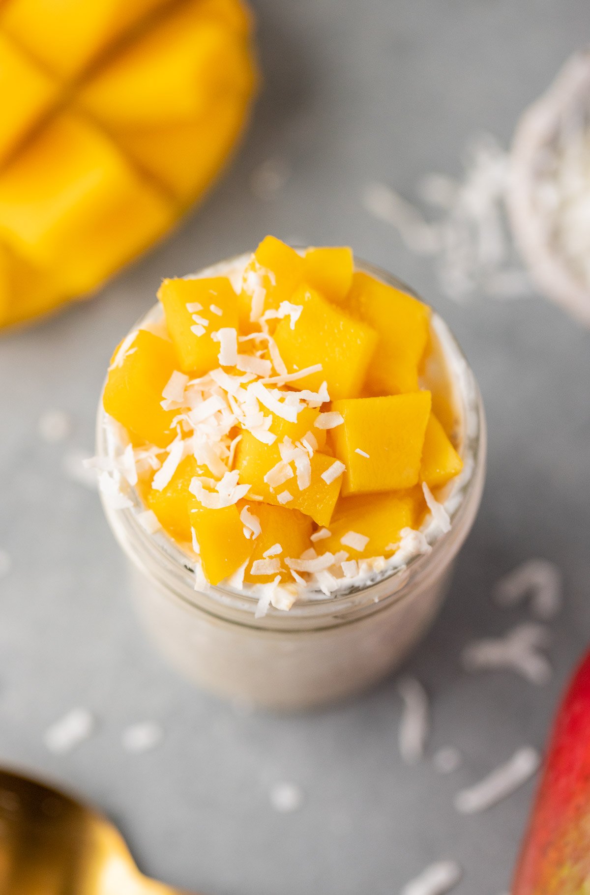 An overhead shot of mango overnight oats in a mason jar with a sliced mango and coconut flakes in the background