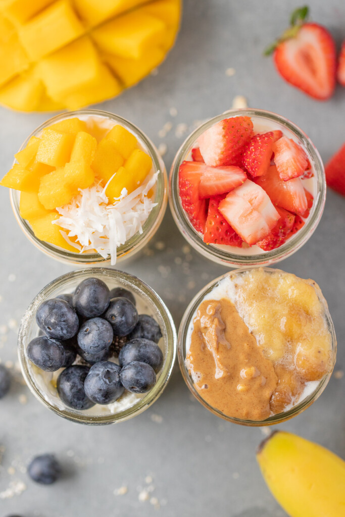 An overhead shot of four mason jars of overnight oats: mango overnight oats, strawberry overnight oats, blueberry overnight oats, banana overnight oats