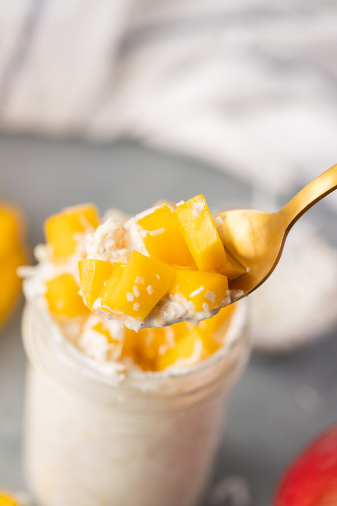 A gold spoon taking a bite out of a mason jar of mango overnight oats