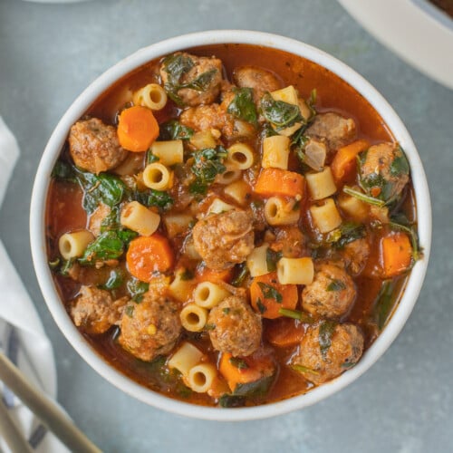 Meatball Soup in a white bowl with a pot and bowl of soup on the side on a grey background