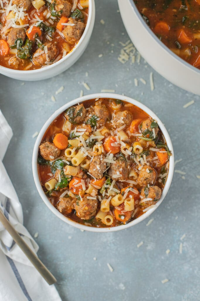 Meatball Soup in a white bowl with a pot and bowl of soup on the side on a grey background
