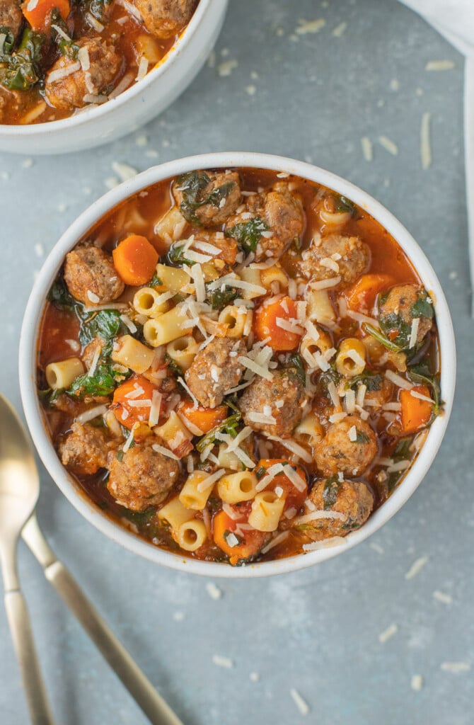 Meatball Soup in a white bowl with a bowl of soup and spoons on the side on a grey background