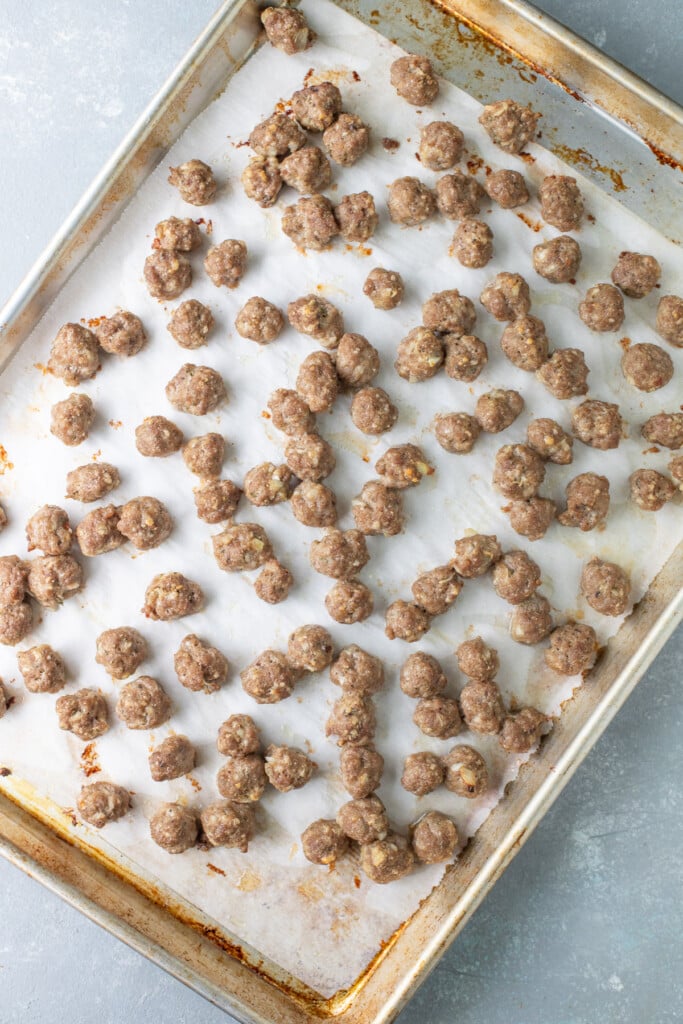 Small Meatballs on a parchment lined baking sheet fully cooked for Italian Meatball Soup on a grey background