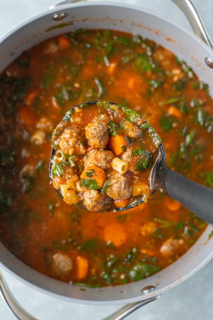 A ladle of Italian Meatball Soup being lifted out of a large pot of the soup in the background