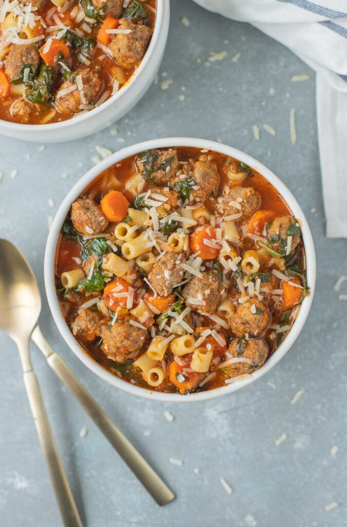 Meatball Soup in a white bowl with a bowl of soup and spoons on the side on a grey background