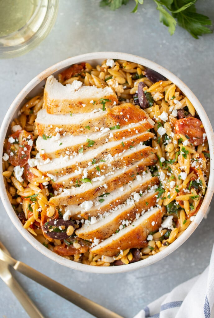 Mediterranean Chicken Orzo on a white dish on a grey background with forks on the side