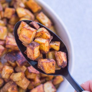 a spoon holding up crispy mexican potatoes from a white bowl
