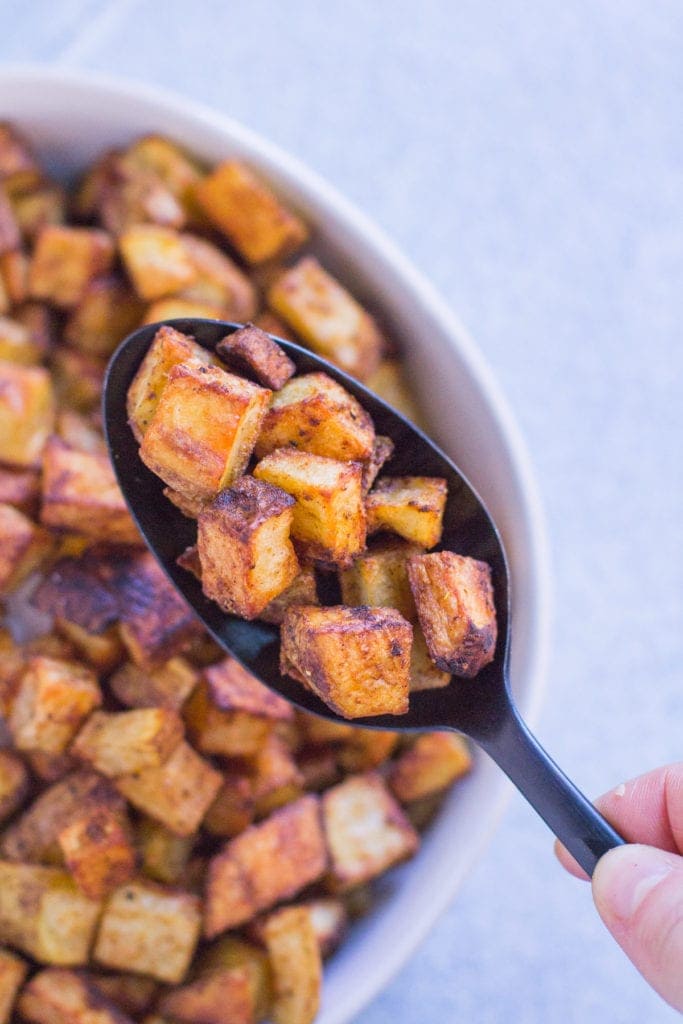 a spoon holding up crispy mexican potatoes from a white bowl