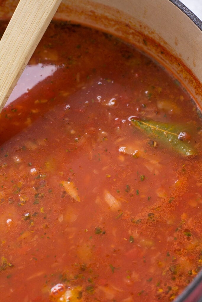a pot of minestrone soup with tomatoes being added to it