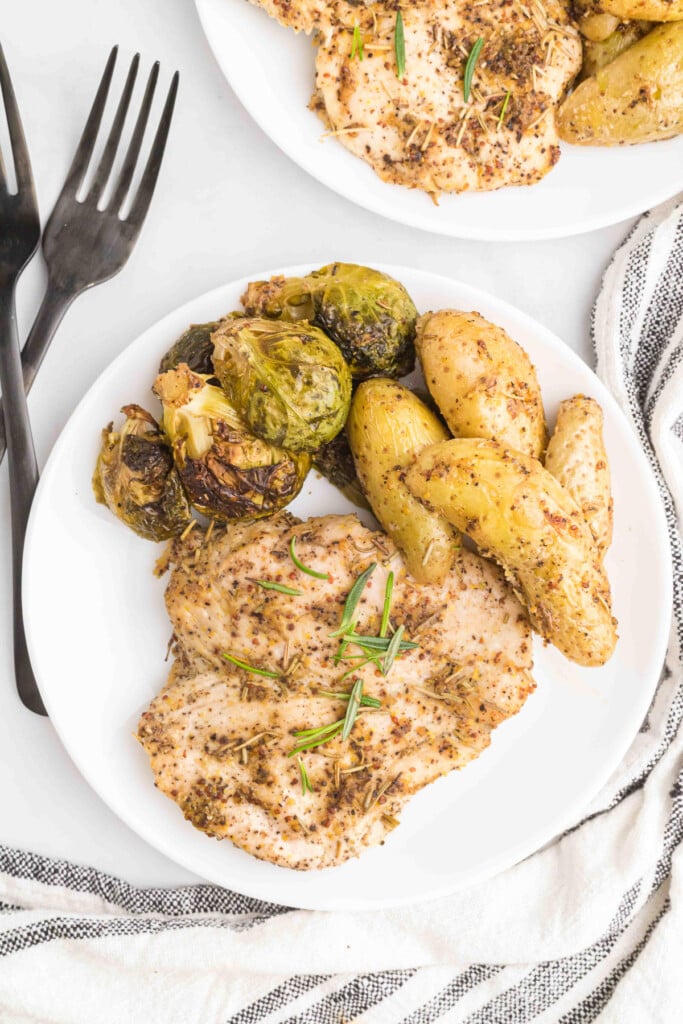 maple mustard chicken on a white plate with brussels sprouts and potatoes on a grey background